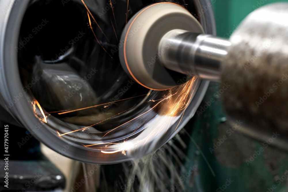 Internal grinding of a part on a CNC machine, sparks and coolant spill over the parts.