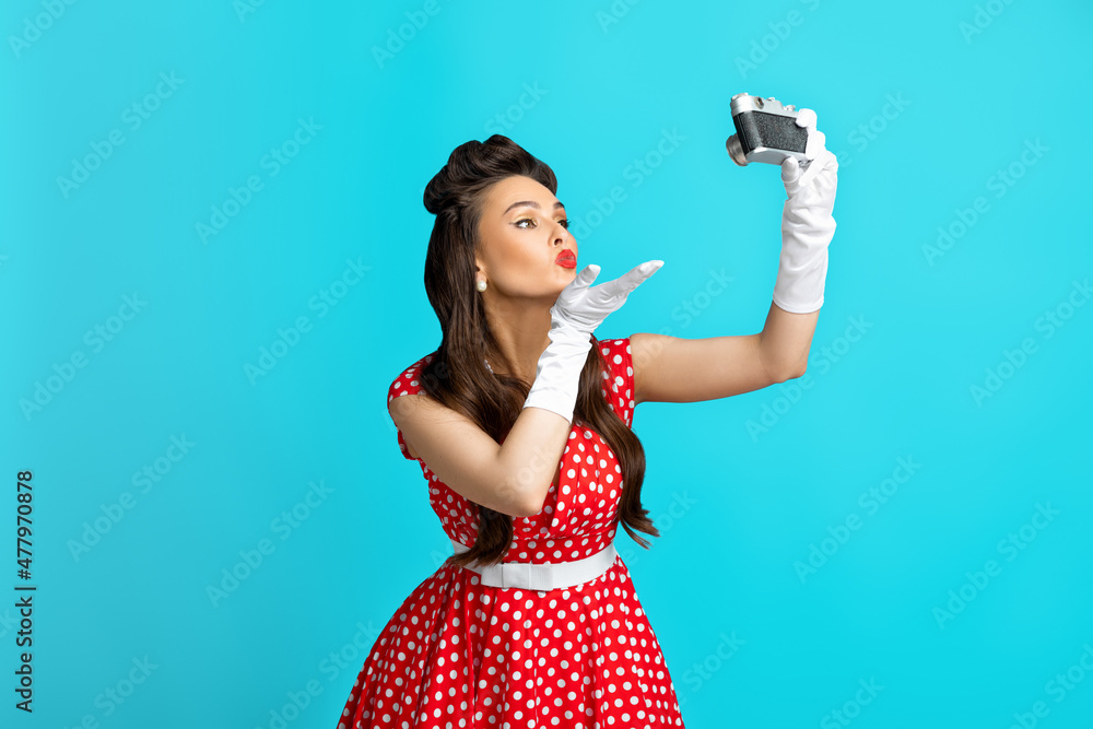 Sexy young pin up lady in polka dot dress taking selfie with retro camera,  blowing air kiss on blue studio background Stock Photo | Adobe Stock