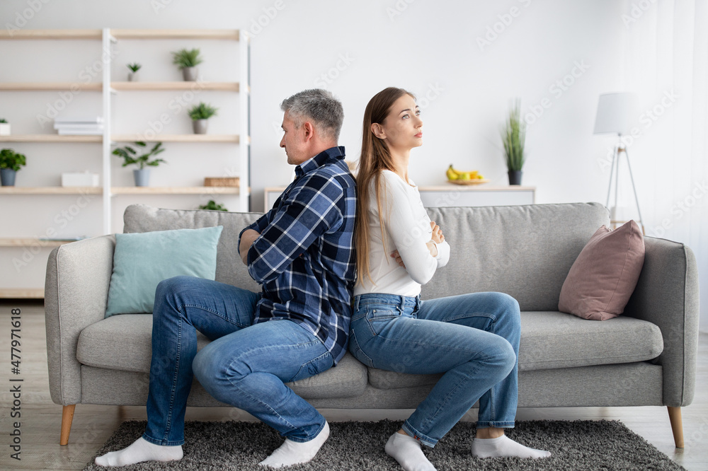 Middle aged married couple sitting back to back on couch, not talking to each other after conflict at home - obrazy, fototapety, plakaty 