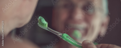 Green toothpaste on toothbrush in hand of senior man looking in mirror photo