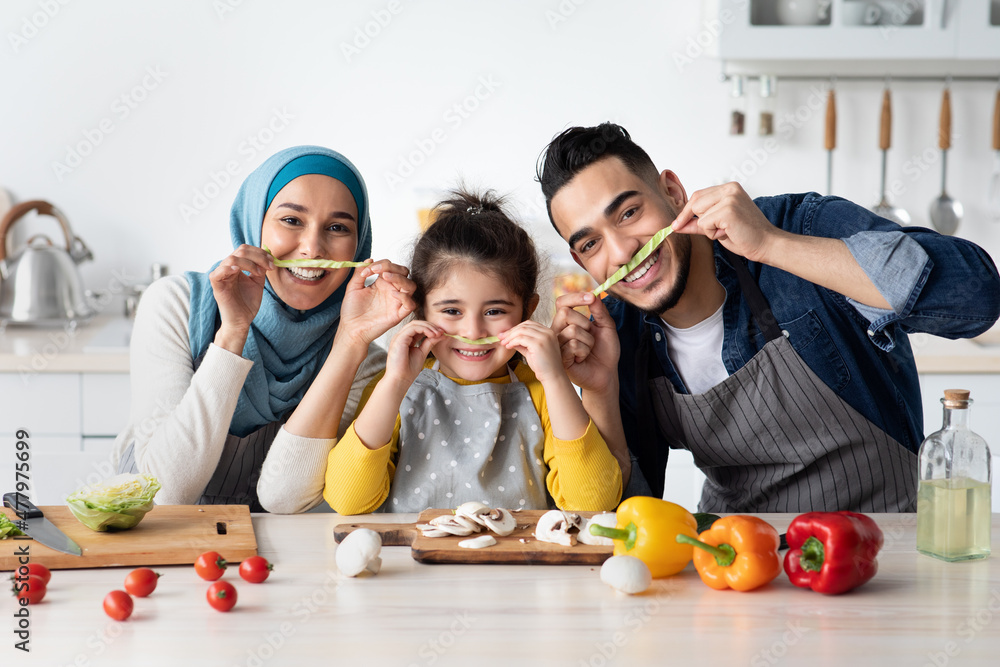 Portrait Of Joyful Muslim Family Of Three Fooling Together In Kitchen