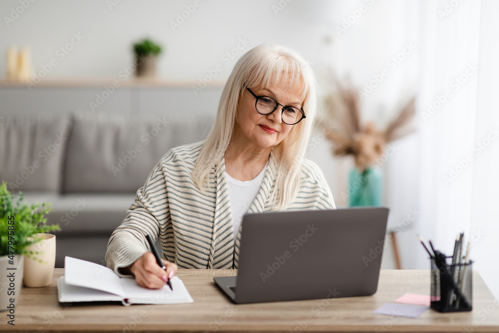 Mature woman writing and using laptop at home