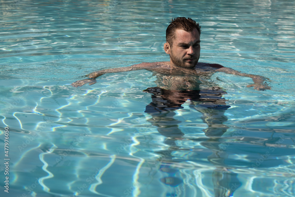 Adult man in blue water of pool. Serious facial expression.