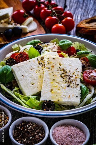 Fresh feta salad - feta cheese, cherry tomatoes, cucumber, black olives and onion on wooden table
