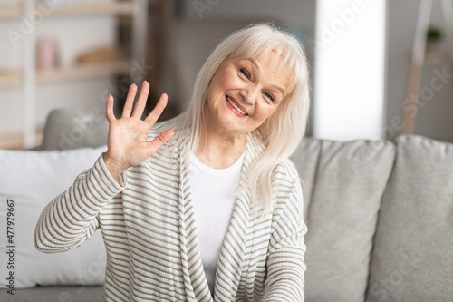 Wallpaper Mural Elderly woman waving at camera and smiling, sitting on sofa Torontodigital.ca