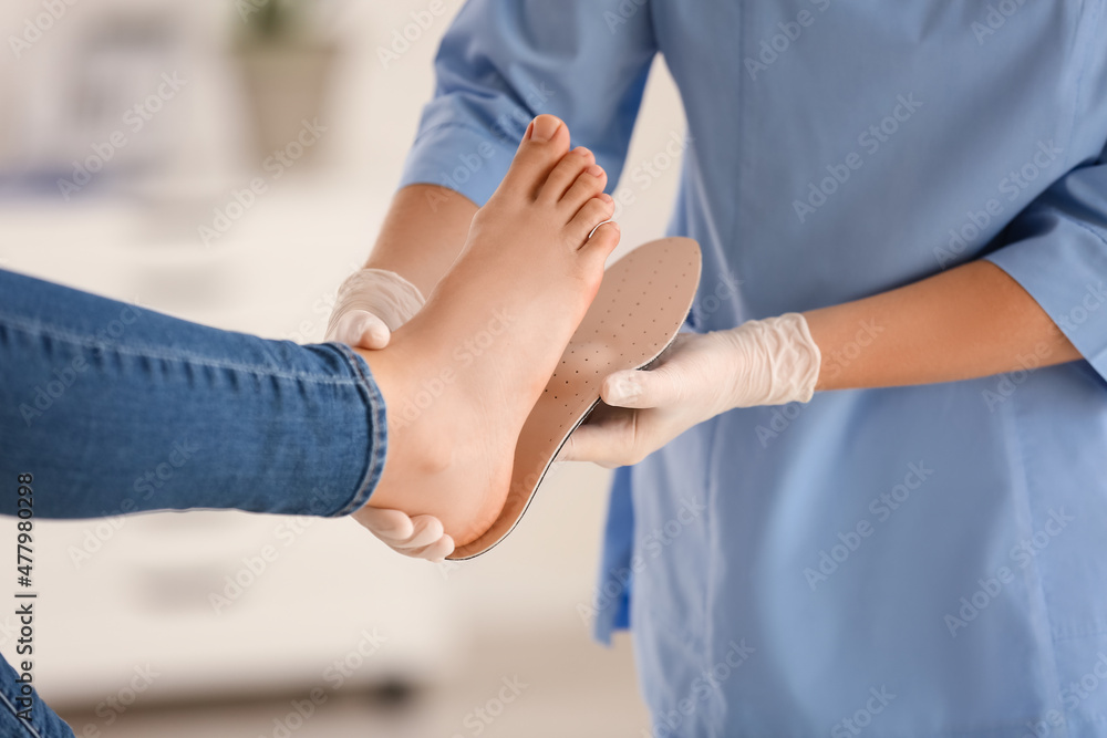 Female orthopedist fitting insole on patient's foot in clinic, closeup Female orthopedist fitting insole on patient's foot in clinic, closeup