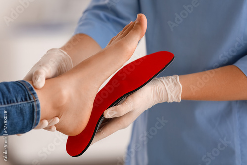Female orthopedist fitting red insole on patient's foot in clinic, closeup
