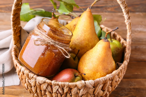 Basket with glass jar of tasty pear jam on wooden background, closeup