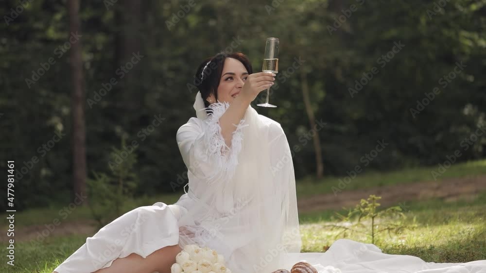 Bride in white boudoir dress sitting in garden, drinking champagne with
