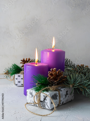 Lilac candles on a light textured table. Gifts  fir branches and cones in the background. Light background. Space for text. Postcard