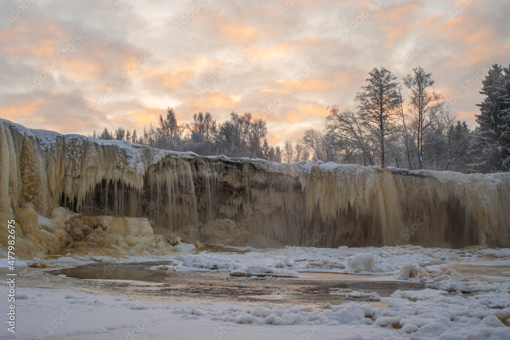 Beautiful frozen Jagala waterfall (Estonian - Jägala) on a cloudy winter morning. Cascading icicles. Beautiful sky in the background.