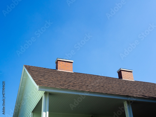 Close up two chimneys bricks on the roof of the light green wooden house against blue sky background on a sunny day with copy space.