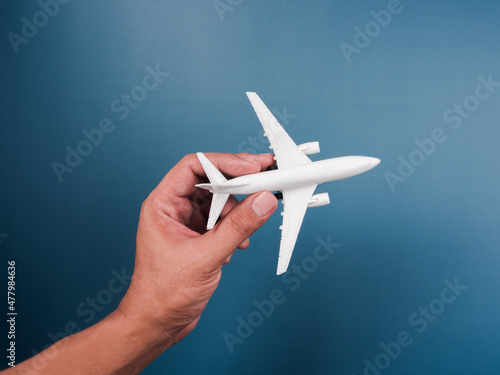 Fototapeta Naklejka Na Ścianę i Meble -  Hand holding white plane toy model on a blue background, top view, minimal style. White airplane, flat lay design. Flight, travel concept.