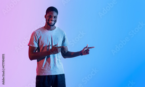 Portrait of athletic black man pointing aside at empty space in neon lighting, banner design