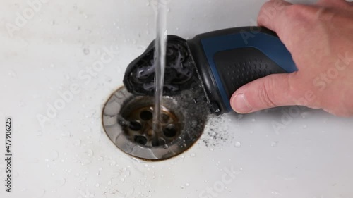cleaning the rotary electric shaver from stubble under the water jet photo