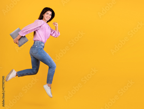Fototapeta Naklejka Na Ścianę i Meble -  Excited young armenian woman running with laptop computer in hand, having fun on yellow studio background, copy space