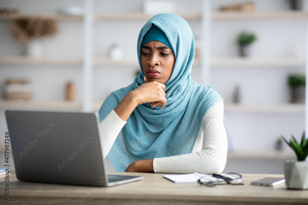 Stressed black muslim freelancer lady looking at laptop screen with worry Stressed black muslim freelancer lady looking at laptop screen with worry