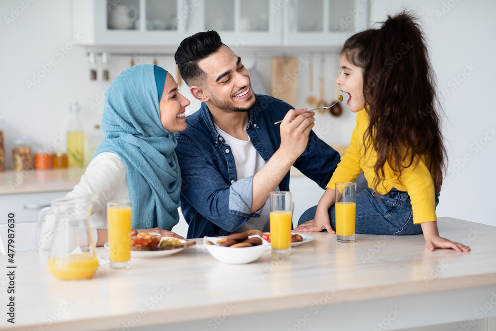 Young Muslim Family Of Three Having Lunch In Kitchen Together Young Muslim Family Of Three Having Lunch In Kitchen Together