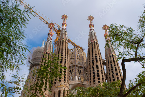 Low angle view of The Basílica de la Sagrada Família also known as the Sagrada Familia in Barcelona city centre. Cloudy sky and crane on a background.