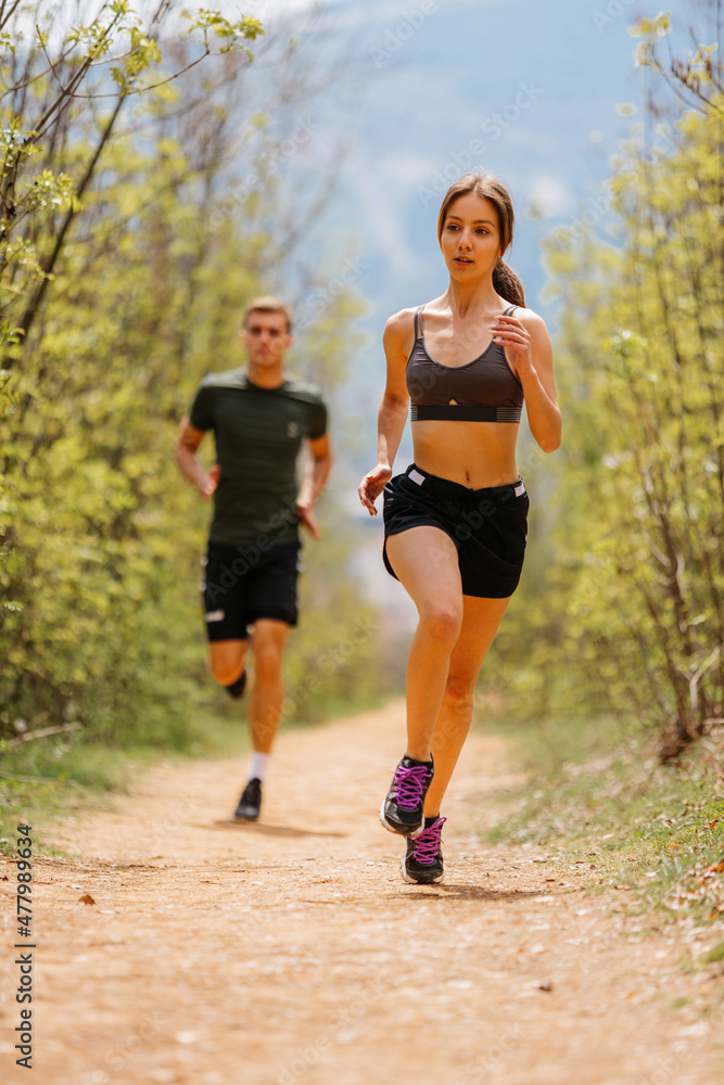 Man and woman exercising and jogging together at the park. Happy and smiling as they run along the path during sunset on a warm summer day Man and woman exercising and jogging together at the park. Happy and smiling as they run along the path during sunset on a warm summer day