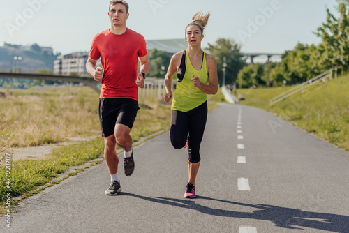 Full-length front view of an attractive caucasian couple running together in a park on a sunny day.. © qunica.com