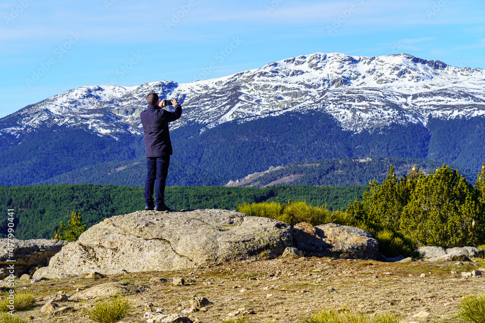 Man climbed on a rock and taking photos with his mobile to the mountains. Morcuera Madrid.