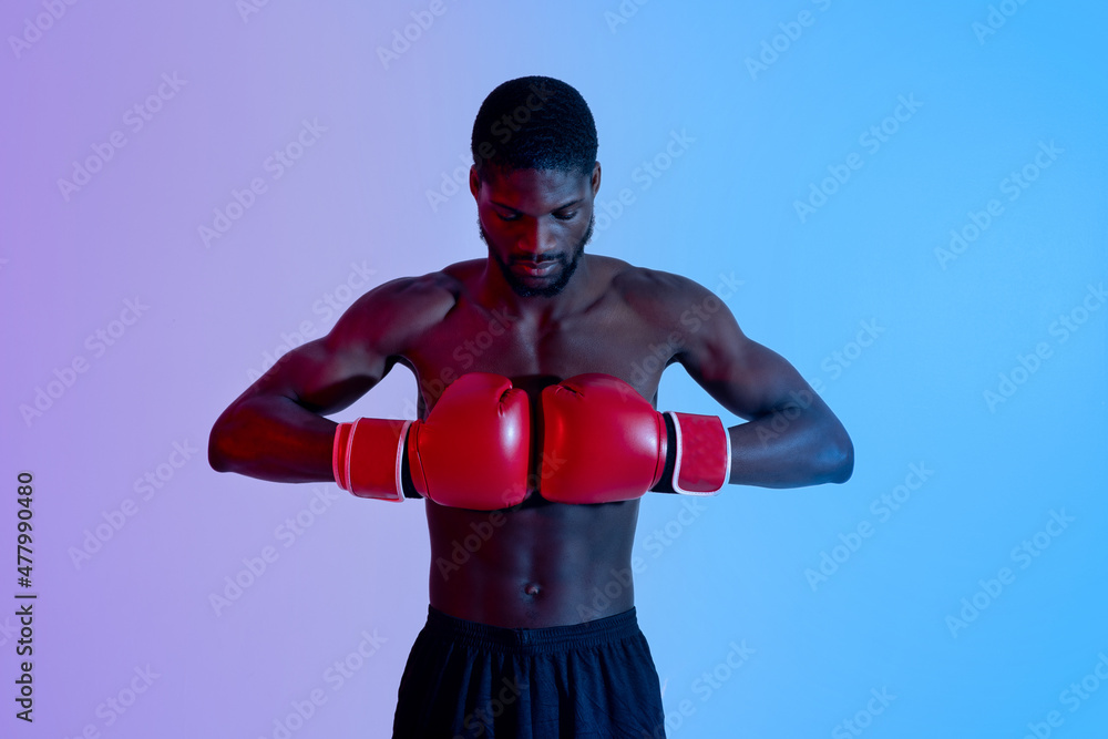 Portrait of motivated black boxer putting gloves together in neon light. Professional sports concept