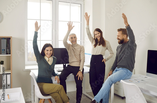 Team of happy, confident, motivated, enthusiastic male and female company employees smiling and raising their hands to vote for a good business suggestion during a casual corporate meeting photo
