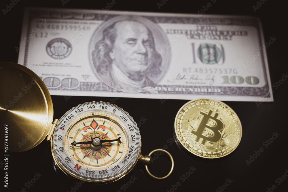 a bitcoin coin lies next to a compass and a hundred dollar bill a bitcoin coin lies next to a compass and a hundred dollar bill