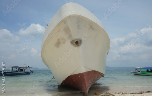 A white ship is being repaired on the shore with small ships sailing in the background
