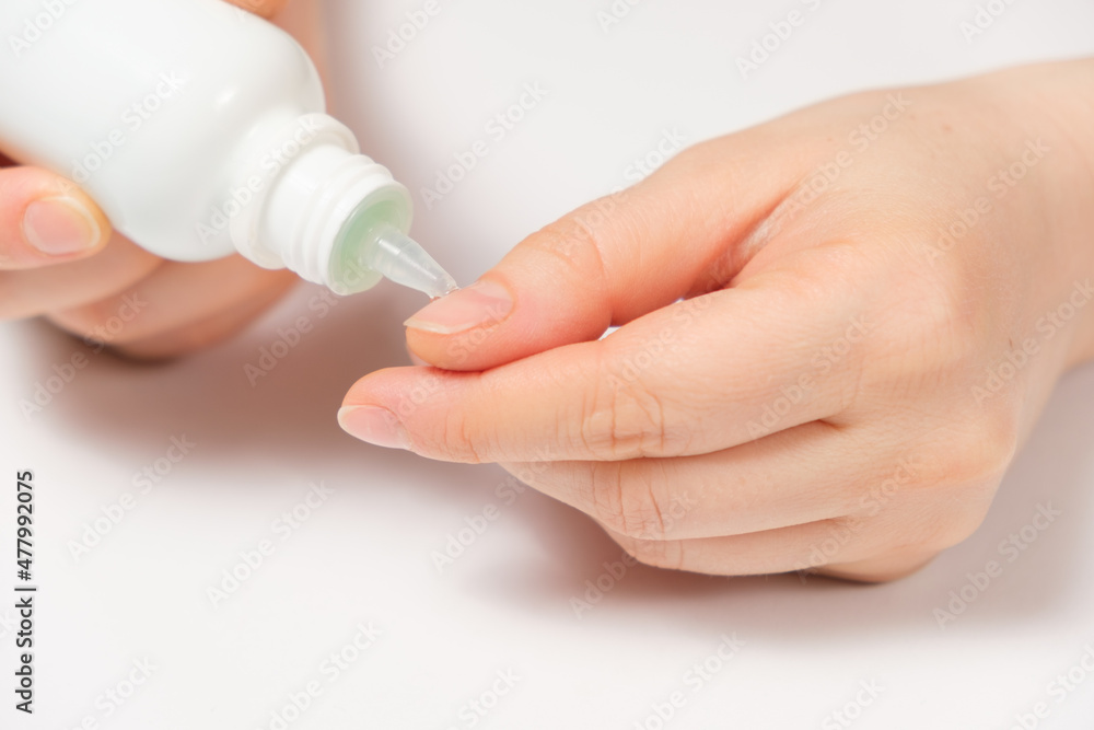Woman applies cuticle remover to nails on white background Woman applies cuticle remover to nails on white background