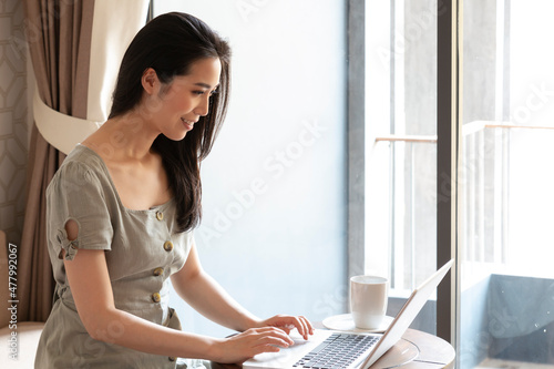 Young female using computer laptop in bedroom. Beautiful young woman using computer laptop in hotelroom working and drinking cup of coffee.