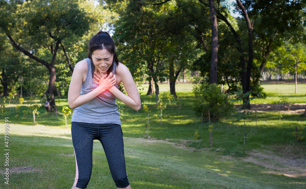 Young female have chest pain while running in the park. Young woman suffering from heart attack outdoors. Female runner suffering painful angina pectoris or asthma breathing problems. Young female have chest pain while running in the park. Young woman suffering from heart attack outdoors. Female runner suffering painful angina pectoris or asthma breathing problems.