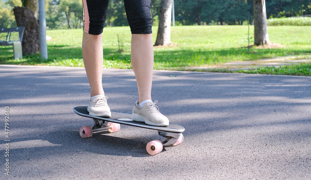 Young teen girl learning to rides a skateboard. Young woman learning skateboarding lesson in the park. Portrait of young female skateboarding in the park. Woman standing and learning to ride skate. Young teen girl learning to rides a skateboard. Young woman learning skateboarding lesson in the park. Portrait of young female skateboarding in the park. Woman standing and learning to ride skate.