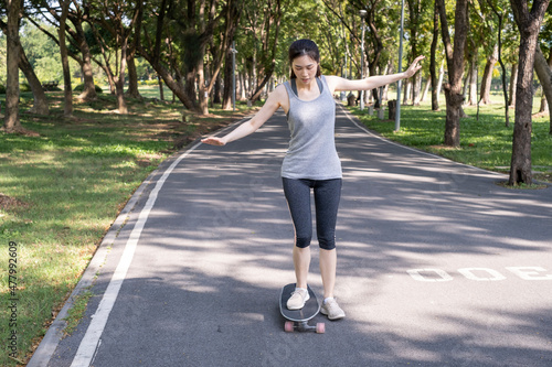 Young teen girl learning to rides a skateboard. Young woman learning skateboarding lesson in the park. Portrait of young female skateboarding in the park. Woman standing and learning to ride skate.