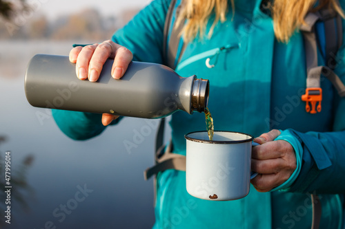 Obraz na plátně Woman is pouring hot drink from thermos into travel mug