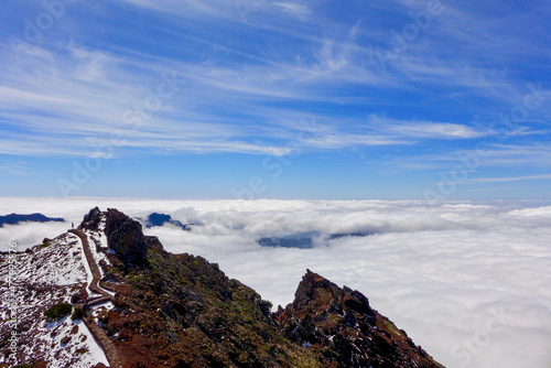 Lone hiker walks the trail at Roque de los Muchachos on a bright, sunny day. The view into the volcano caldera is covered in a cloud inversion. Caldera de Taburiente National Park, La Palma, Spain