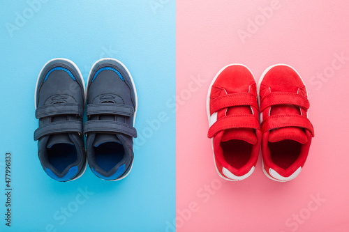 Red and dark blue sport shoes for little boy and girl on light blue pink table background. Pastel color. Children footwear. Closeup. Top down view.