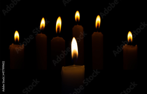 Burning candles in the dark on a black background. Religious rites, holidays or burials are accompanied by burning candles.