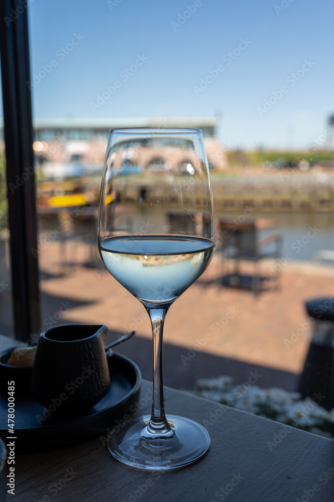 Glass of white wine served in cafe with view on harbour of Harlingen, vacation in Friesland, Netherlands Glass of white wine served in cafe with view on harbour of Harlingen, vacation in Friesland, Netherlands