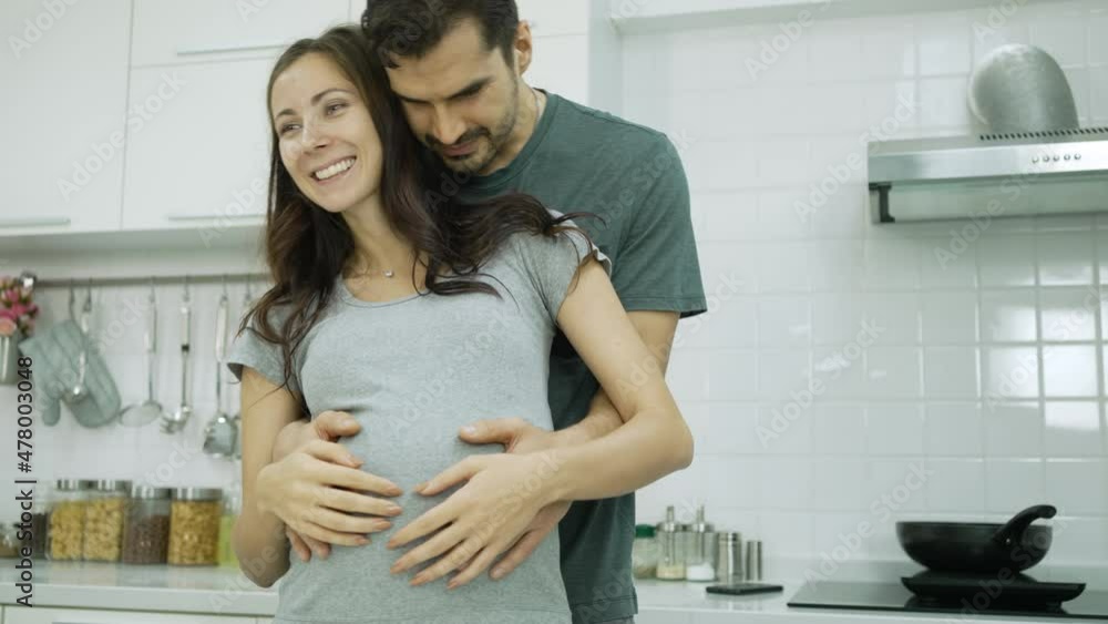 caucasian man hugging his pregnant wife in kitchen caucasian man hugging his pregnant wife in kitchen