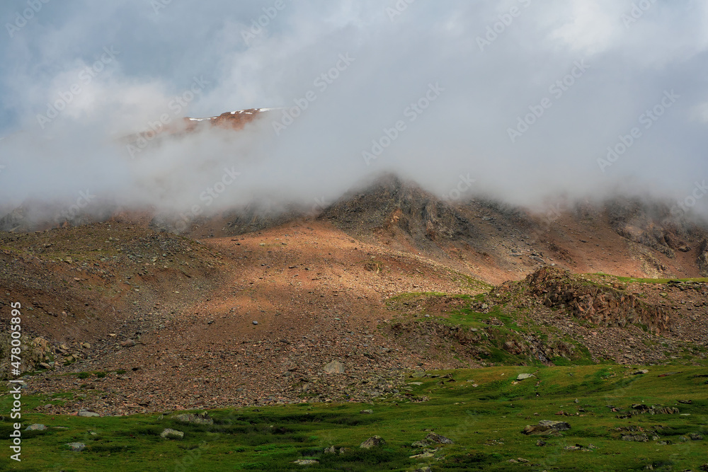 Dramatic fog among giant rocky mountains. Ghostly atmospheric view to big cliff. Low clouds and beautiful rockies. Minimalist scenery mysterious place.
