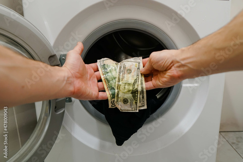 Frustrated man getting out clothes with wet money dollar banknotes from washing machine.
