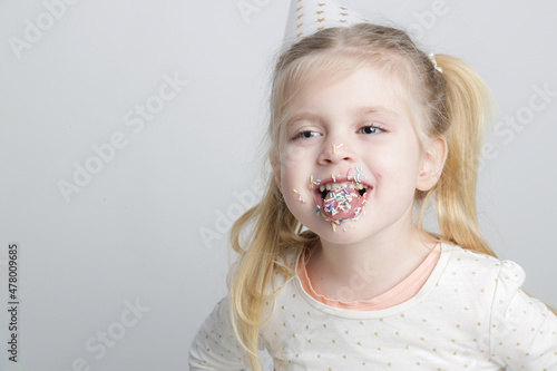 Cute little birthday girl with colorful sugar sprinkles on lips and in mouth. Children and sugar addiction concept.