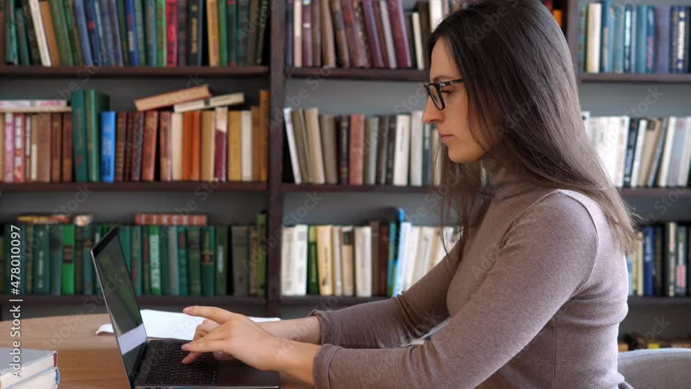 College student uses a laptop to watch online distance learning, a seminar, a distance university webinar, or conduct a virtual classroom meeting in the university's creative space. The girl works on College student uses a laptop to watch online distance learning, a seminar, a distance university webinar, or conduct a virtual classroom meeting in the university's creative space. The girl works on