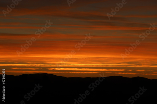 horizonte de nubes rojas y naranjas con puesta del sol y siluetas de monta  as