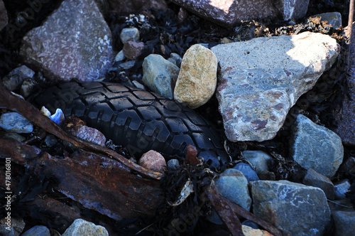 Rusty scrap metal and rubber tire on the beach. Seaweeds and boulders. Horizontal image.
