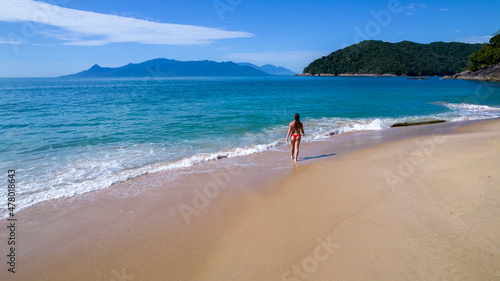 Brazilian woman in bikini on a deserted beach in Ubatuba, São Paulo, Brazil. Playing in the sea water Atlantic forest, yellow sand and clear sea water. Figueira beach paradise.
