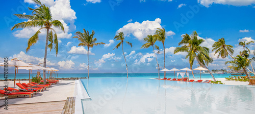 Amazing outdoor tourism landscape. Luxurious beach resort with swimming pool seaside beach chairs or loungers under umbrellas with palm trees and blue sky. Summer travel hotel and vacation background 