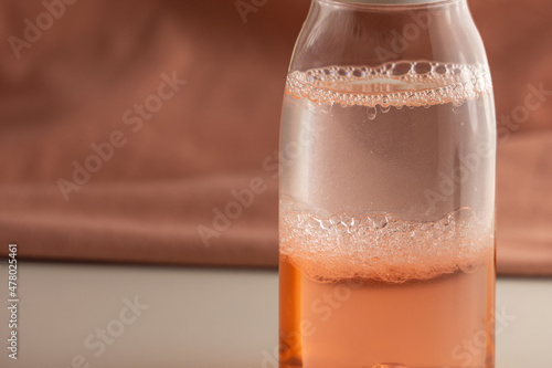 Bubbling Bi-Phase Makeup Remover. Mixing of two liquids of different density and color. Bottle with two-color liquid on a pink background.